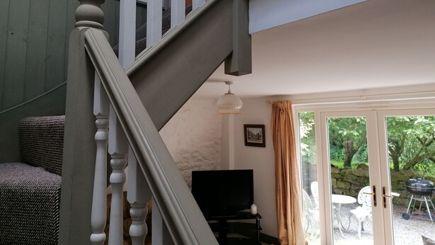 A staircase with white balusters leading to a living area with a television and a wicker sofa. - Countryside Cottage Retreat at Ty'r Cwm Farm (Ammanford)
