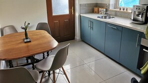 A compact kitchen with a wooden dining table, blue cabinets, and a coffee maker. - Countryside Cottage Retreat at Ty'r Cwm Farm (Ammanford)