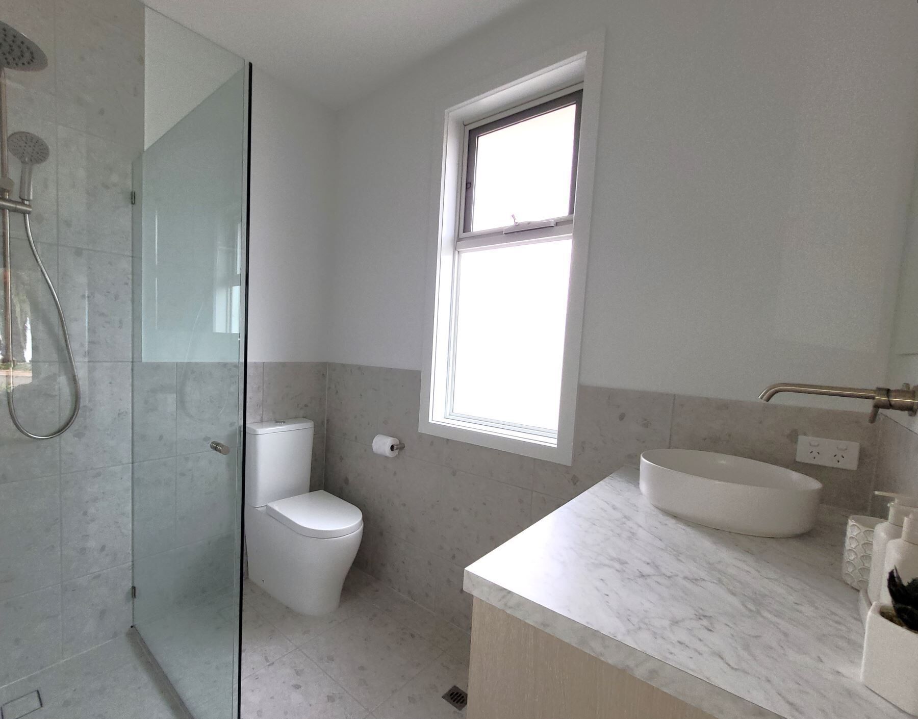 A bathroom with a glass-enclosed shower, a toilet, a sink, and a window providing natural light.