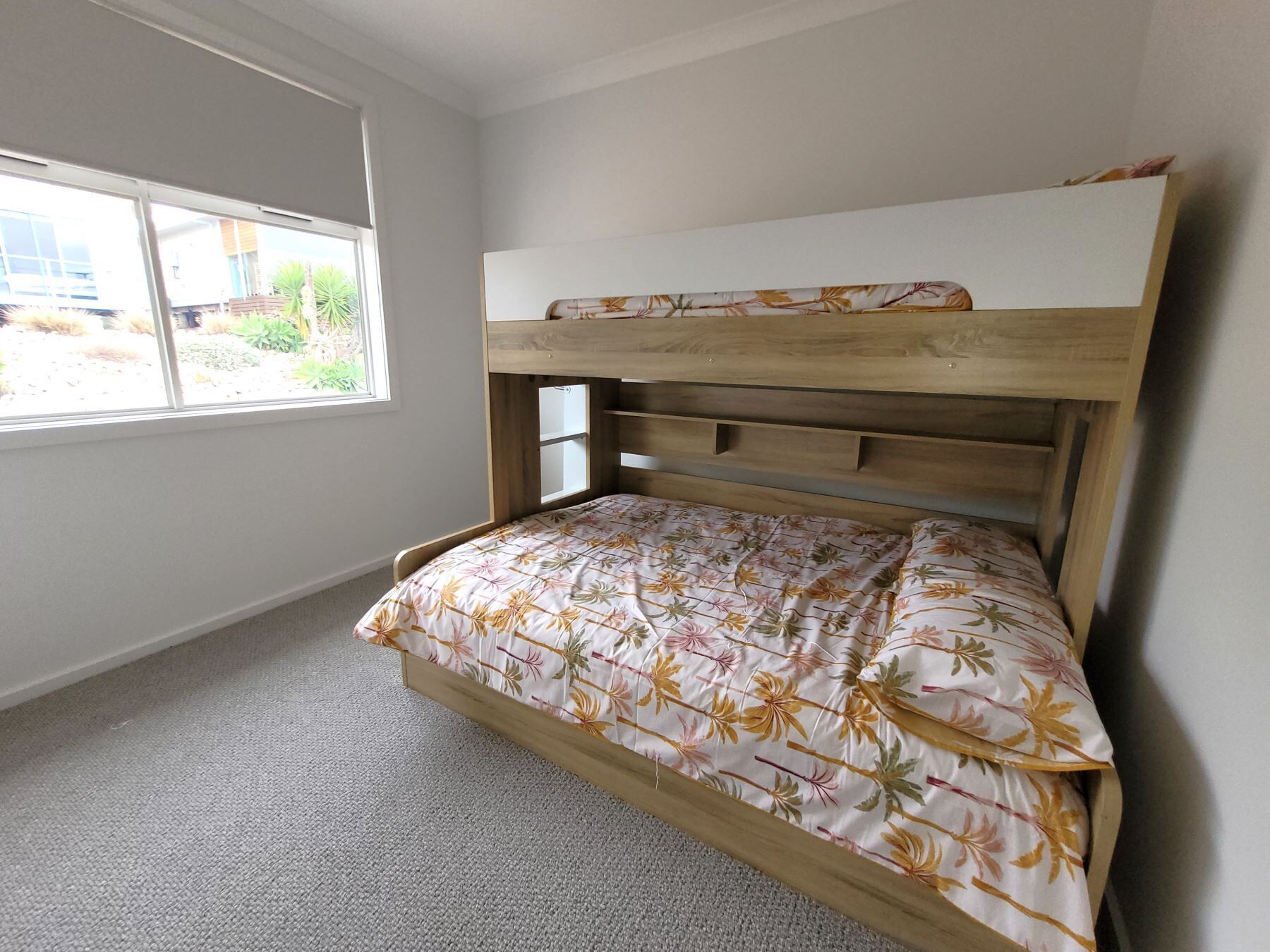 A bedroom with a bunk bed, a window with a view of greenery, and a carpeted floor.