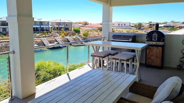 A balcony with a table, chairs, a grill, and a view of a marina and buildings. - Happy Days, Wallaroo (Wallaroo)
