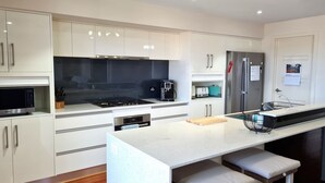 A modern kitchen with white cabinetry, a stainless steel refrigerator, a built-in oven, and a large island with bar stools. - Happy Days, Wallaroo (Wallaroo)