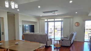 A spacious living area with a wooden dining table, cushioned seating, and a large sliding glass door leading to an outdoor patio. - Happy Days, Wallaroo (Wallaroo)