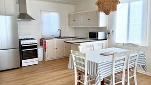 Une cuisine avec des meubles blancs, une cuisinière, un four et un four à micro-ondes. On y trouve une table à manger avec des chaises et un luminaire suspendu.