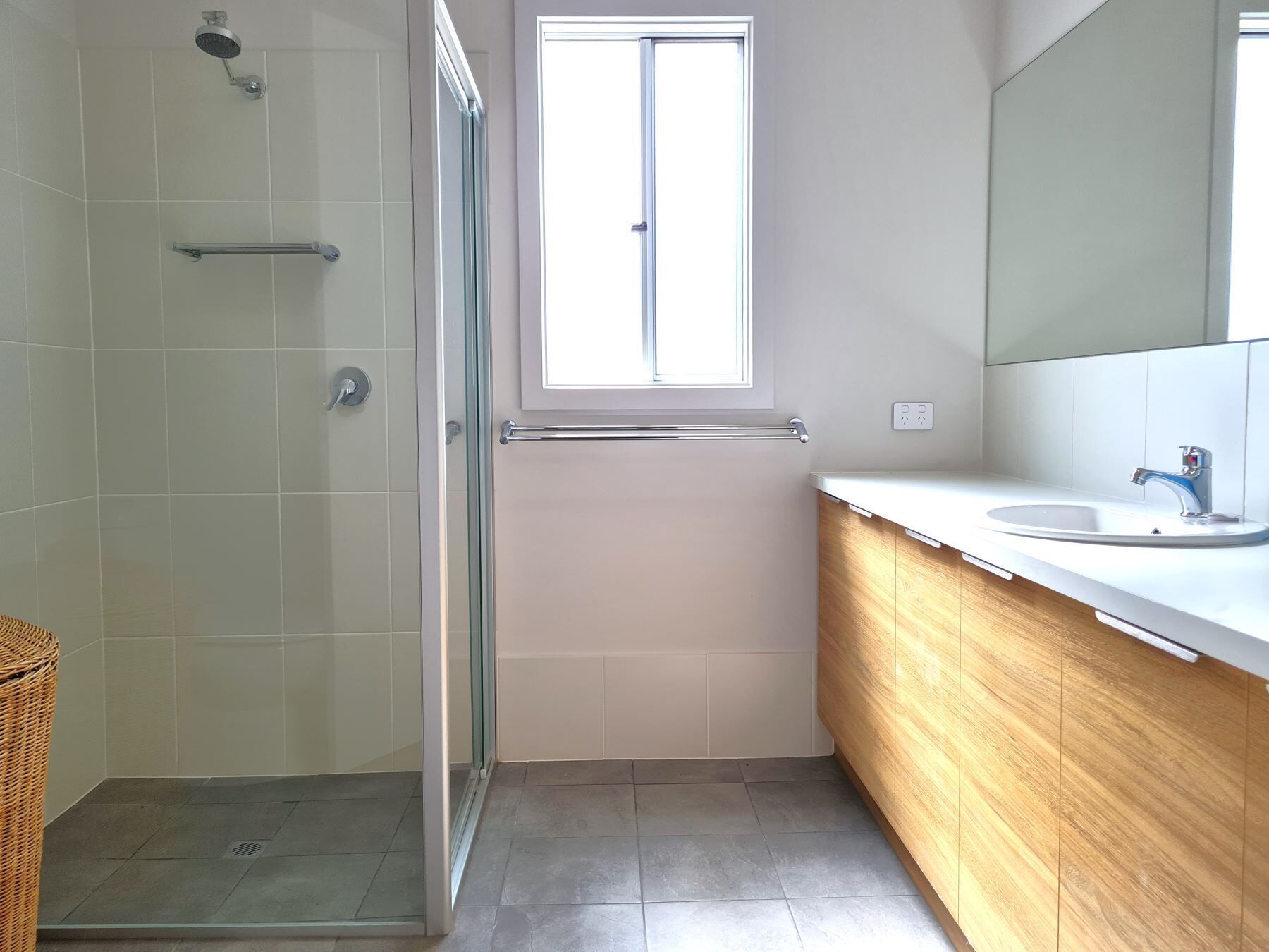 A modern bathroom with a glass shower enclosure, a window, a sink, and a wooden vanity.