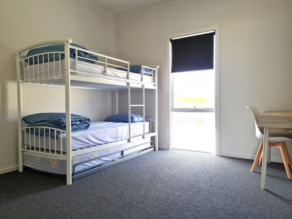 Quarto com beliche, escrivaninha, cadeira, piso coberto por carpete e janela com persianas.