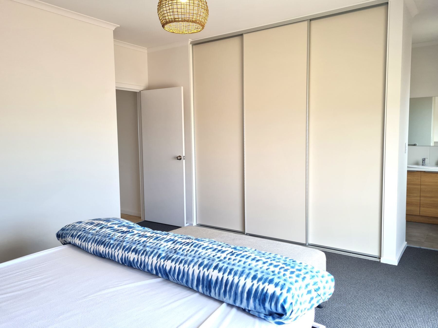 A hotel room with a bed, a wardrobe, and a bathroom visible through an open door.
