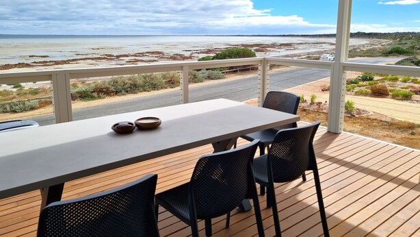 A covered outdoor seating area with a table and chairs, overlooking a beach and road. - Beachfront Beauty, Moonta Bay (Moonta Bay)