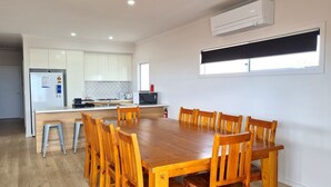 A modern kitchen with white cabinets, a wooden dining table, and a built-in oven. - Beachfront Beauty, Moonta Bay (Moonta Bay)