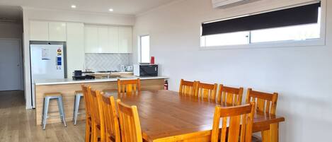 A modern kitchen with white cabinets, a wooden dining table, and a built-in oven.
