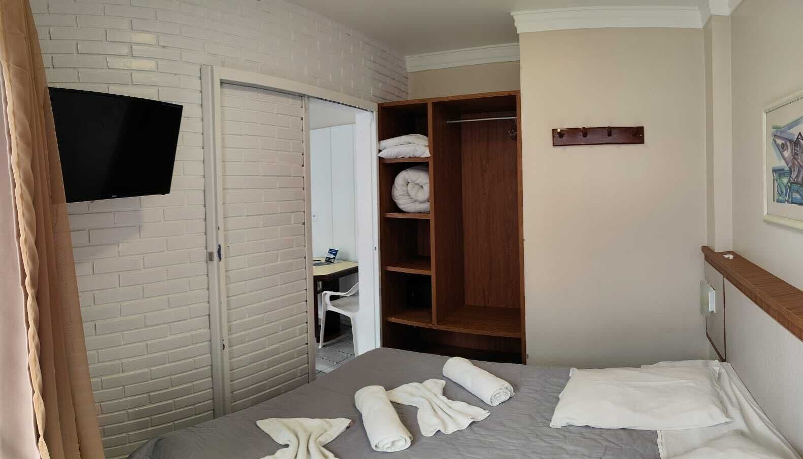 Habitación de hotel con cama, armario, escritorio con silla y televisor de pantalla plana montado en la pared.