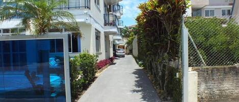 A residential street with modern buildings, a clear sky, and a pathway lined with plants.