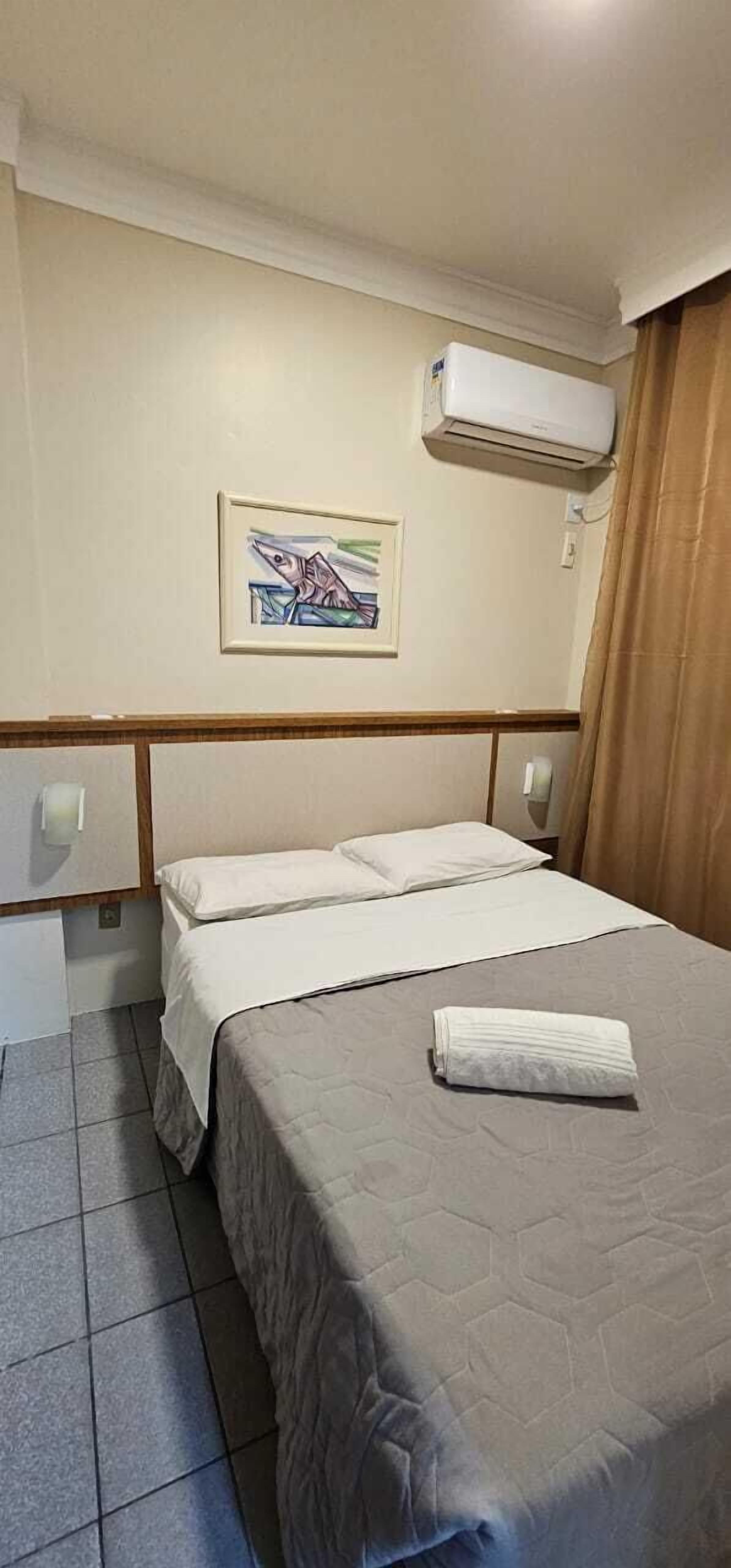 Ein Hotelzimmer mit einem Bett, einem Bild an der Wand und einer Klimaanlage.