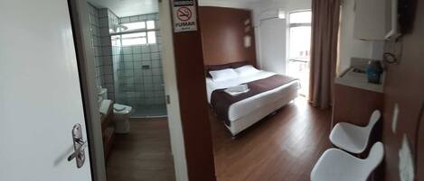 Habitación de hotel con cama, baño con ducha y un cartel que prohíbe fumar.