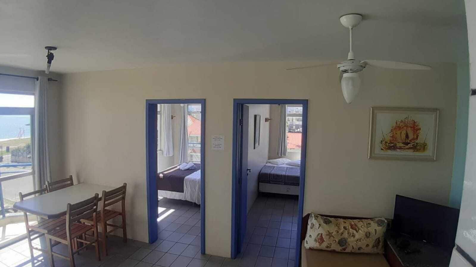 Ein Zimmer mit Esstisch, Stühlen, einem Bett und einem Deckenventilator. Zwei Türen führen in einen weiteren Raum und auf einen Balkon.