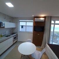 Cocina compacta con lavamanos, microondas y armarios, una pequeña mesa de comedor con sillas y un televisor montado en un panel de madera.