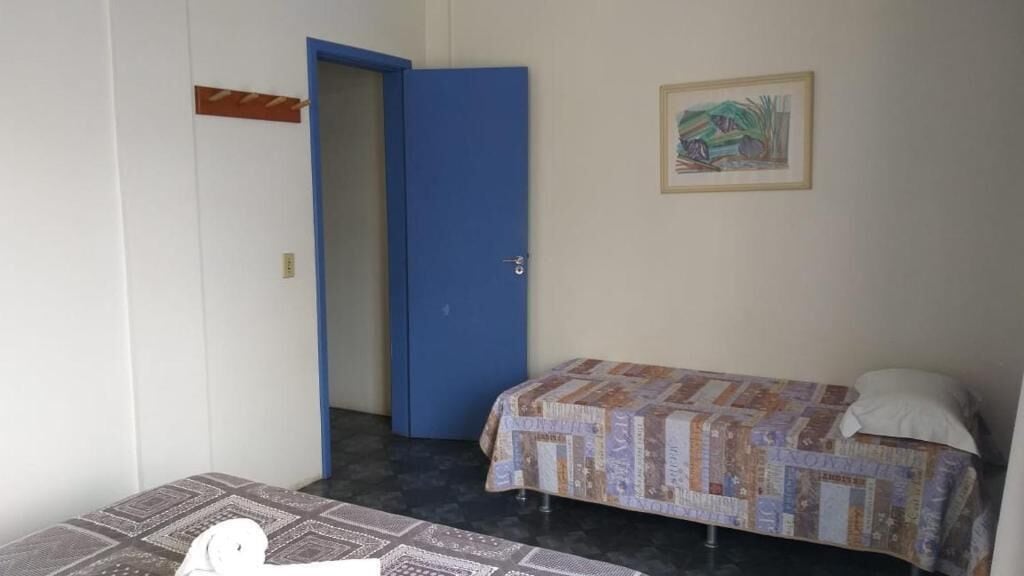 A small room with a bed, a blue door, and a painting on the wall.