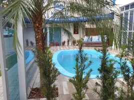 Una piscina interior con solárium de baldosas, rodeada de plantas en macetas y una palmera.