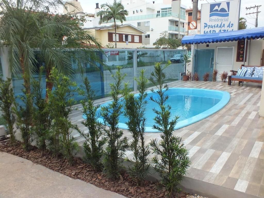 A residential building with a swimming pool surrounded by small trees and a tiled patio.