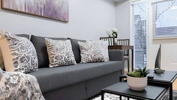 Una sala de estar moderna con un sofá gris, cojines estampados, una mesa de centro con una planta y un cuadro en la pared.