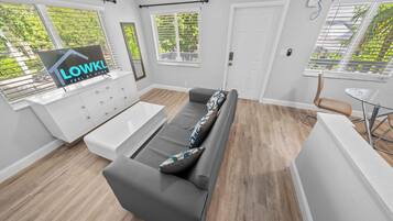 Ein modernes Wohnzimmer mit einem grauen Sofa, einem weißen Couchtisch und einem Essbereich mit einem Glastisch und Metallstühlen.
