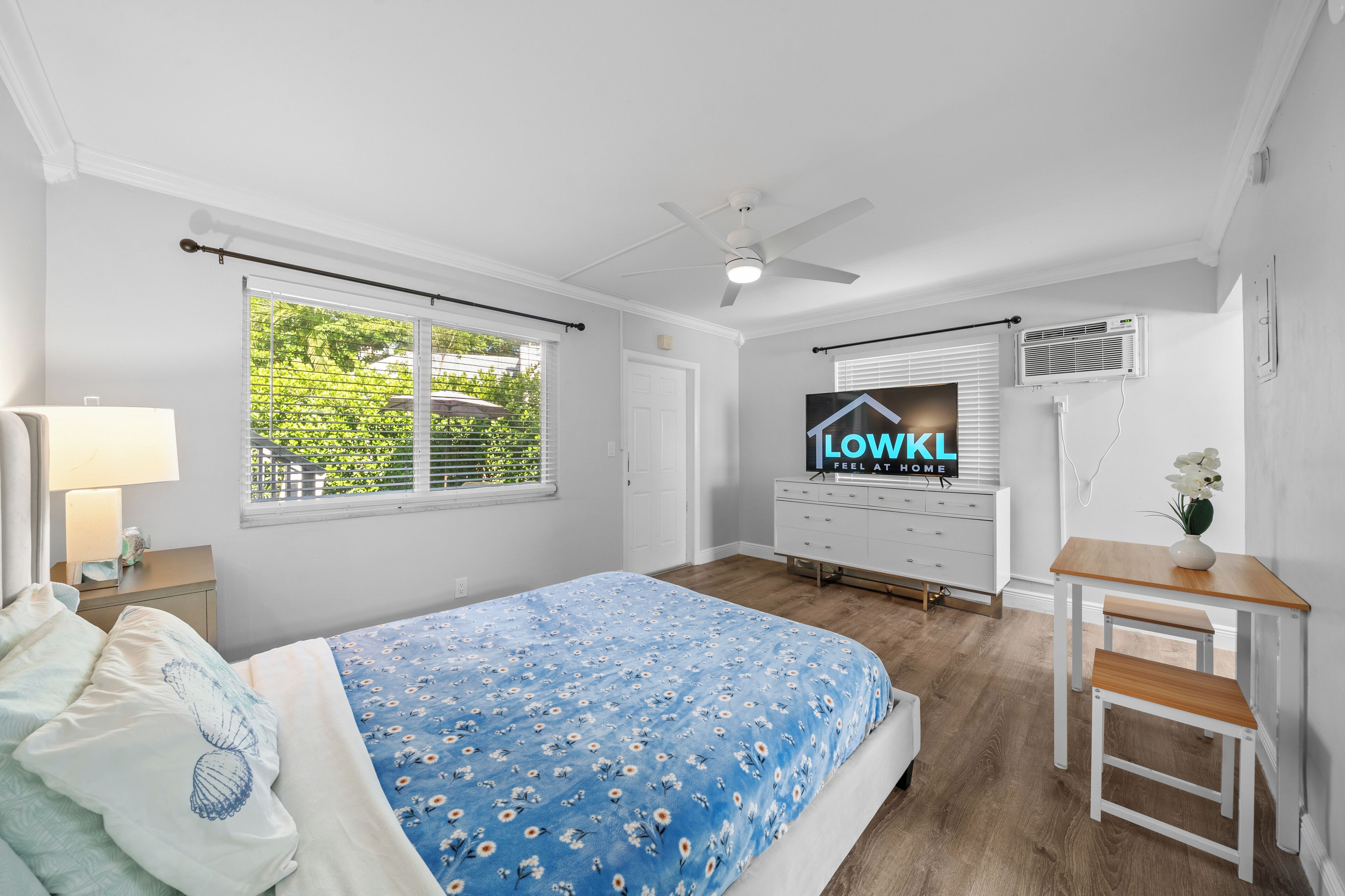 Ein Schlafzimmer mit Bett, Schreibtisch, Deckenventilator und Fenster mit Jalousien.
