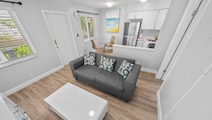 A modern living room with a grey sofa, white coffee table, and a dining area with a small table and chairs. - Riverbend by Lowkl (Fort Lauderdale)
