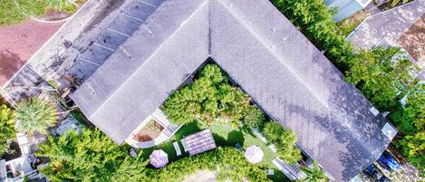 An aerial view of a building with a unique angular roof, surrounded by lush greenery and a parking area.