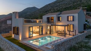 A modern two-story house with a swimming pool, large glass doors, and a stone wall surrounding the property. - Amazing home in Majkovi with sauna (Majkovi)