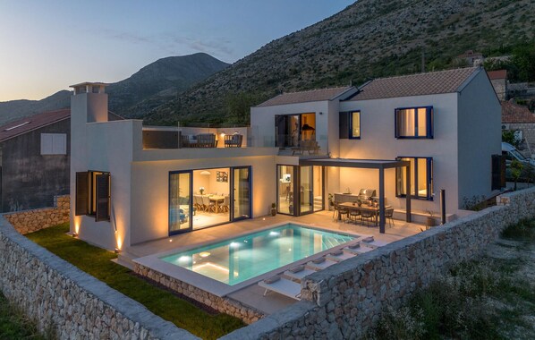 A modern two-story house with a swimming pool, large glass doors, and a stone wall surrounding the property. - Amazing home in Majkovi with sauna (Majkovi)