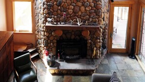 A stone fireplace with a chandelier, a framed picture above it, and a wreath on the wall. - Log Lodge near Colo Springs Just Updated New Toilets, Smart TVs & Lauren bedding (Colorado Springs)