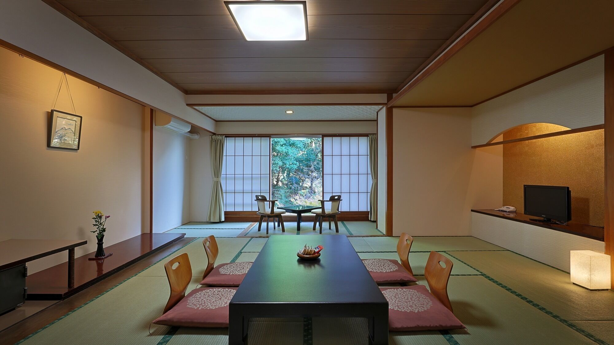 A traditional Japanese room with tatami flooring, a low table with cushions, and sliding doors leading to a view of greenery.