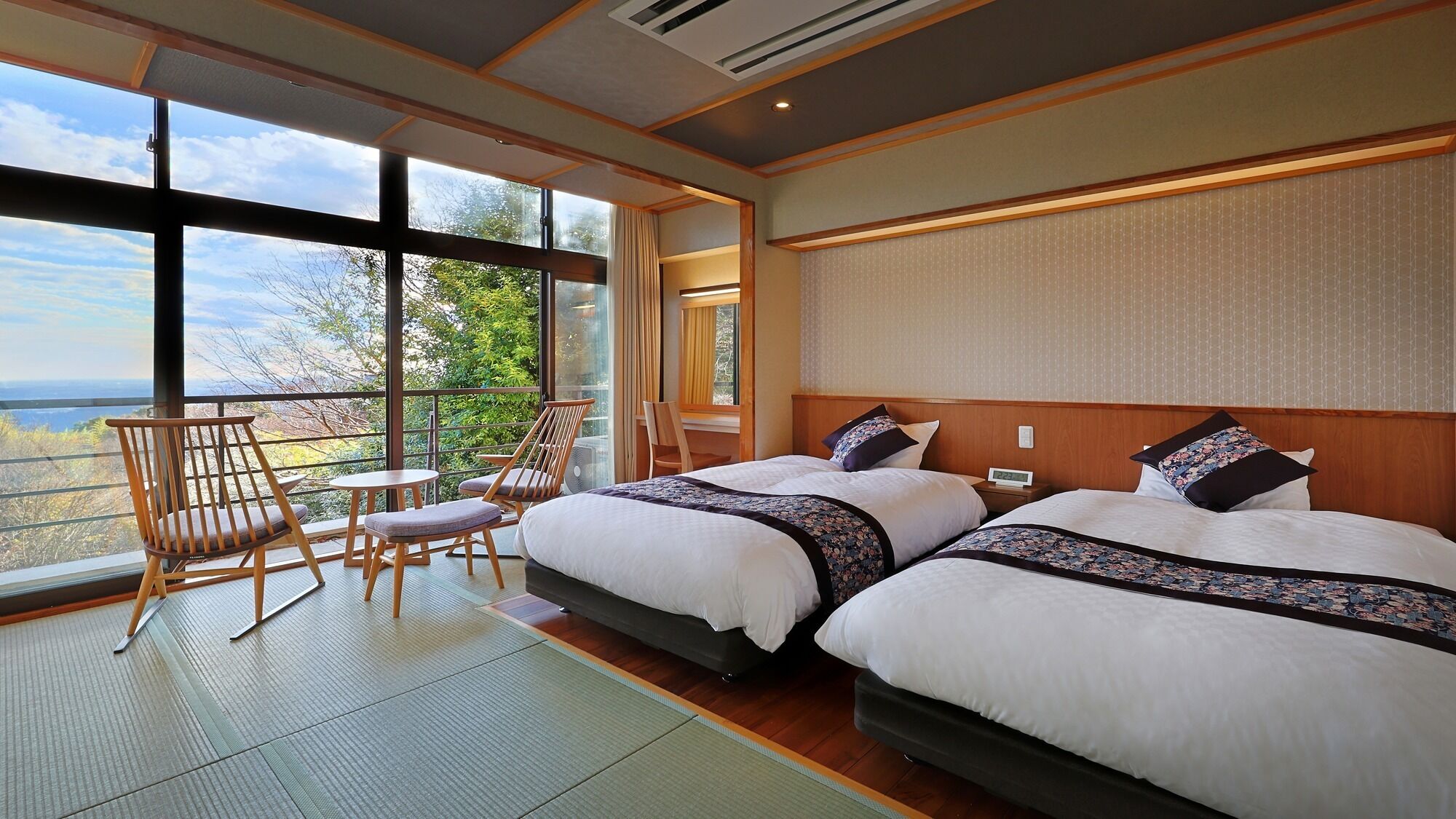 A hotel room with two beds, a balcony with a view, and a seating area with chairs and a table.