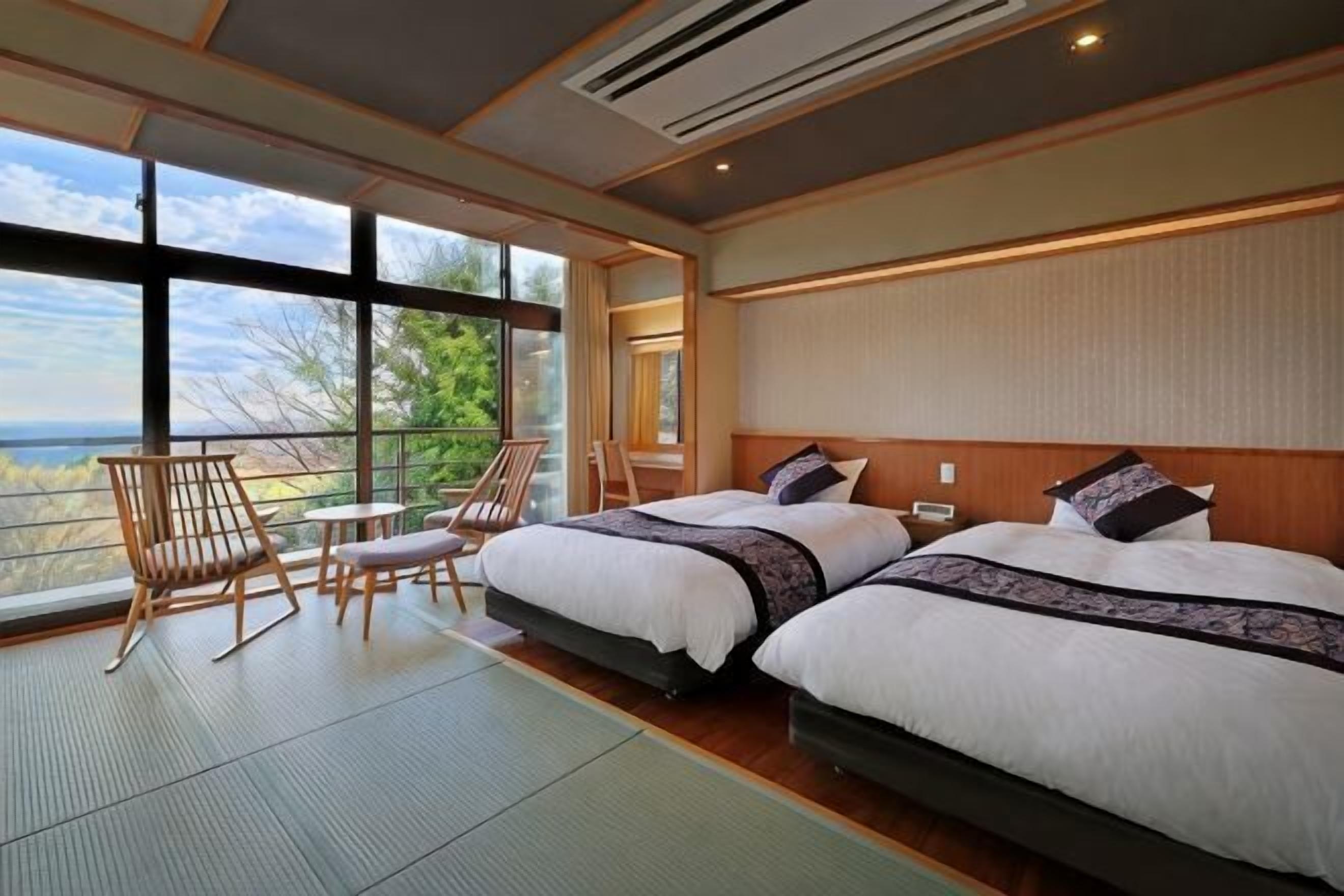 A hotel room with two beds, a balcony with a view, and a seating area with chairs.