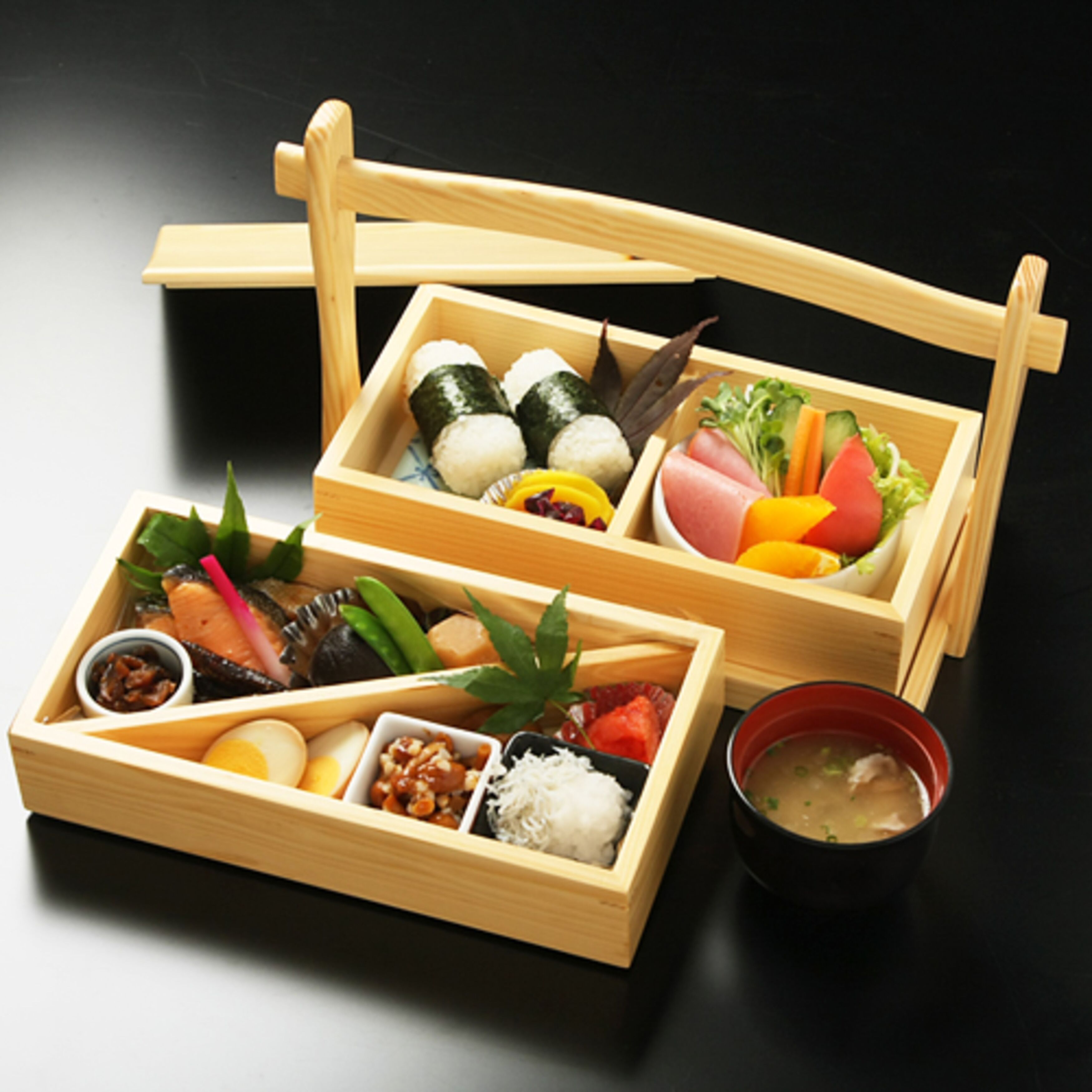 Un plateau en bois contenant divers aliments, notamment des sushis, des légumes et un bol de soupe.