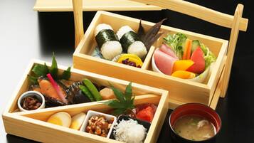 Un plateau en bois contenant divers aliments, notamment des sushis, des légumes et un bol de soupe.