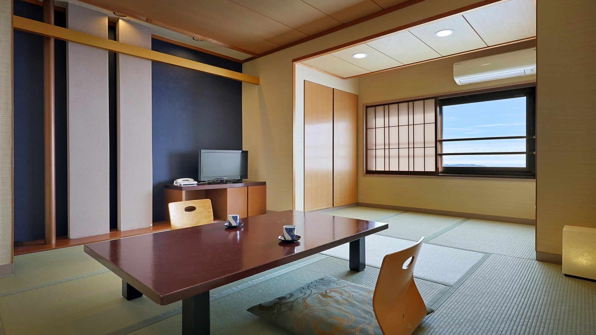 Una habitación con suelo de tatami, una mesa baja, un televisor y puertas correderas.