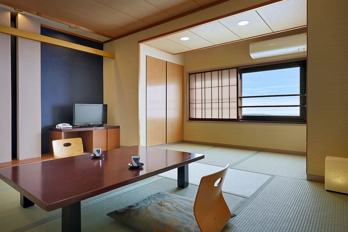 Una habitación con suelo de tatami, una mesa baja, un televisor y puertas correderas.