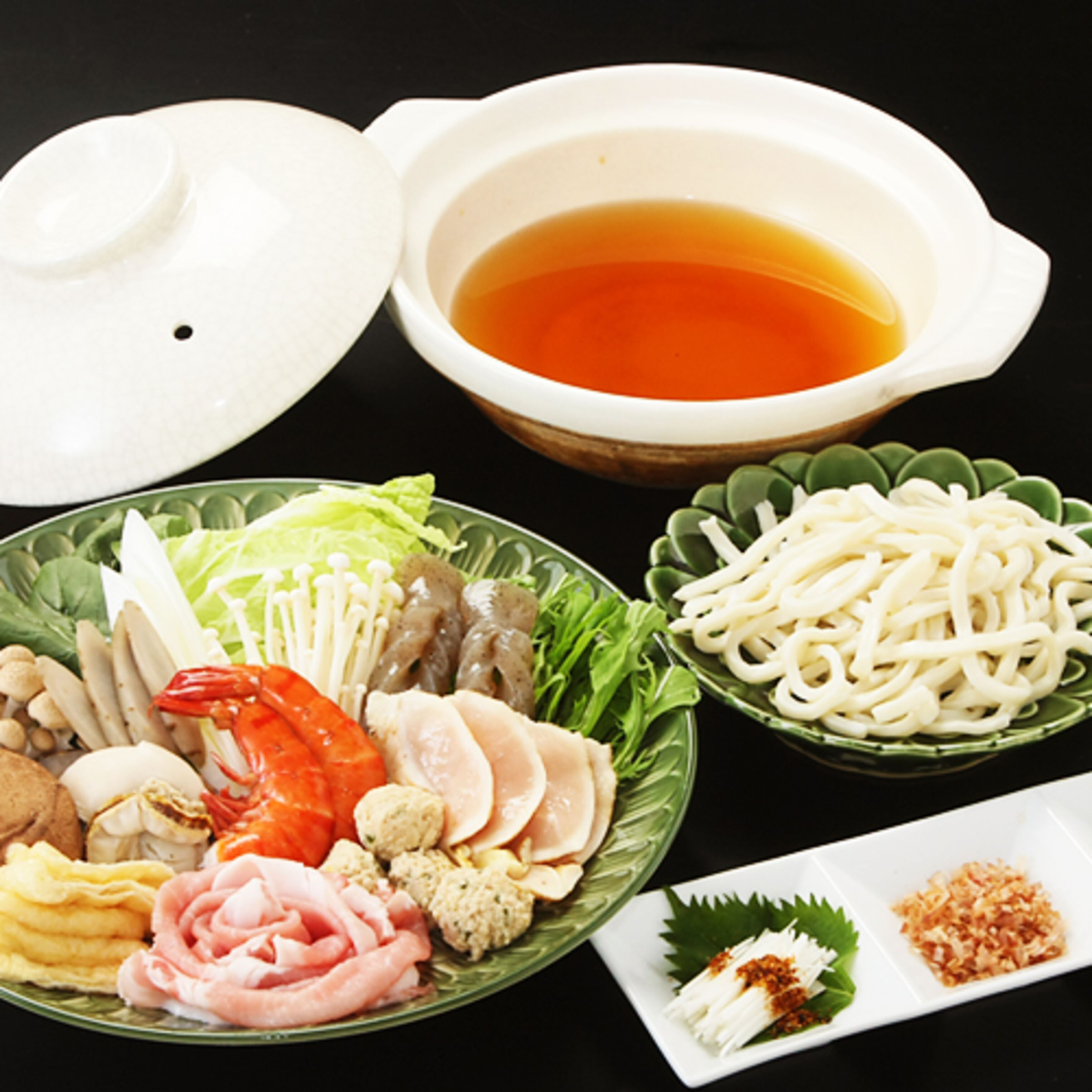 A variety of dishes including noodles, seafood, and vegetables, served on a black table.