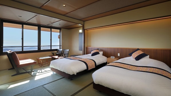 Habitación de hotel con dos camas, un área de descanso con sillas, una mesita y un gran ventanal con vistas.