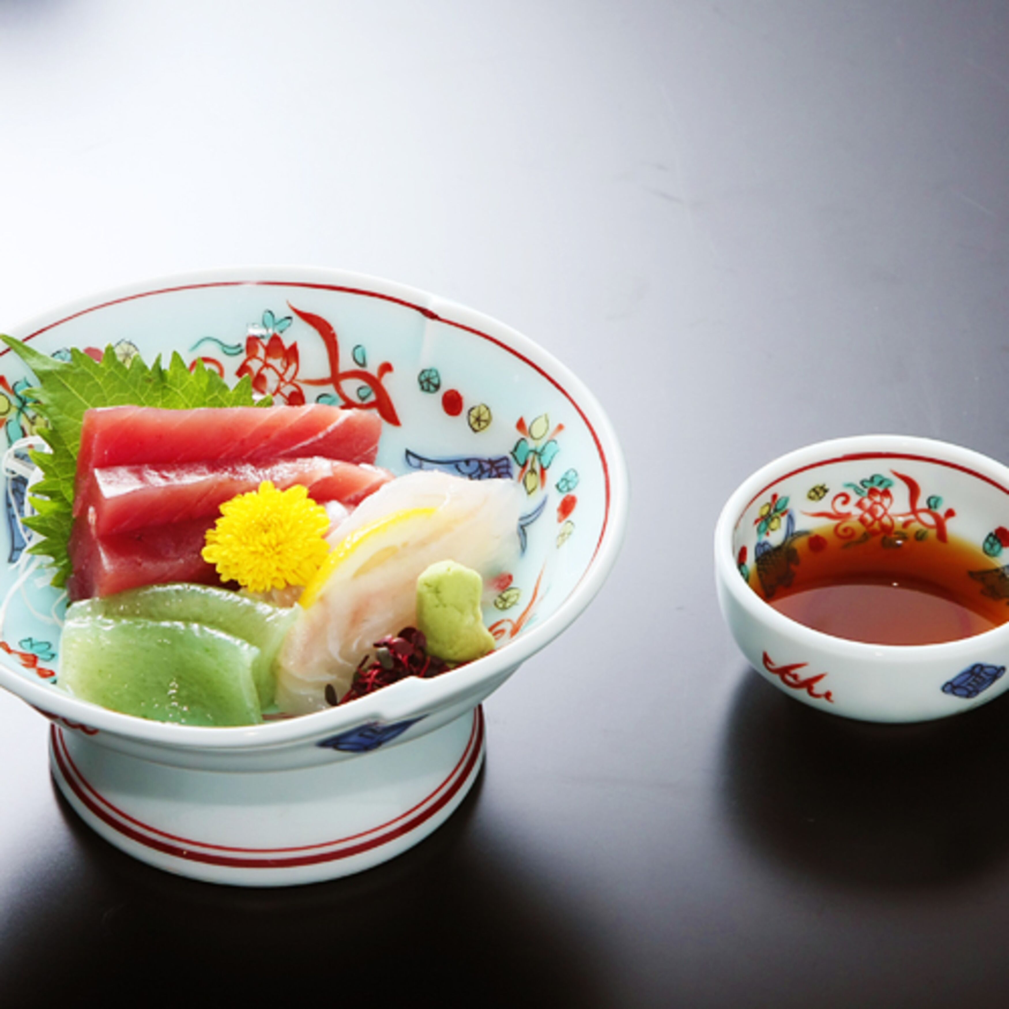 A bowl of sashimi with a small bowl of soy sauce beside it.