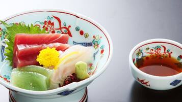 A bowl of sashimi with a small bowl of soy sauce beside it.