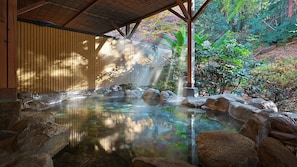 Un área de aguas termales con una terraza de madera, una piscina de piedra y vegetación circundante.