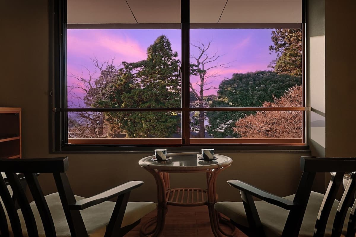 A room with a large window, two chairs, a small table, and a television.