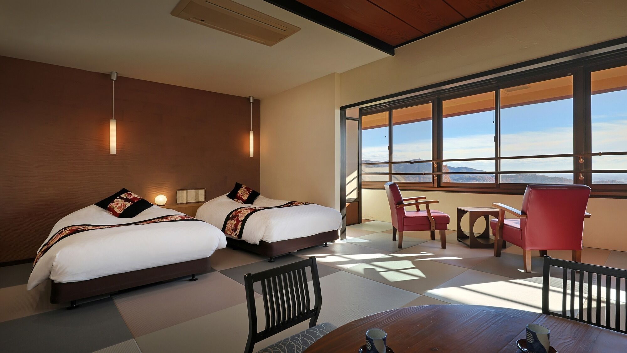 Une chambre d’hôtel avec deux lits, une table à manger, des chaises et de grandes fenêtres donnant sur une vue sur les montagnes.