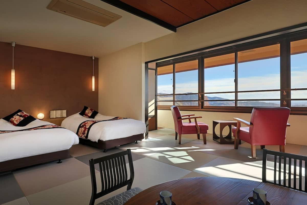 A hotel room with two beds, a dining table, chairs, and large windows offering a mountain view.