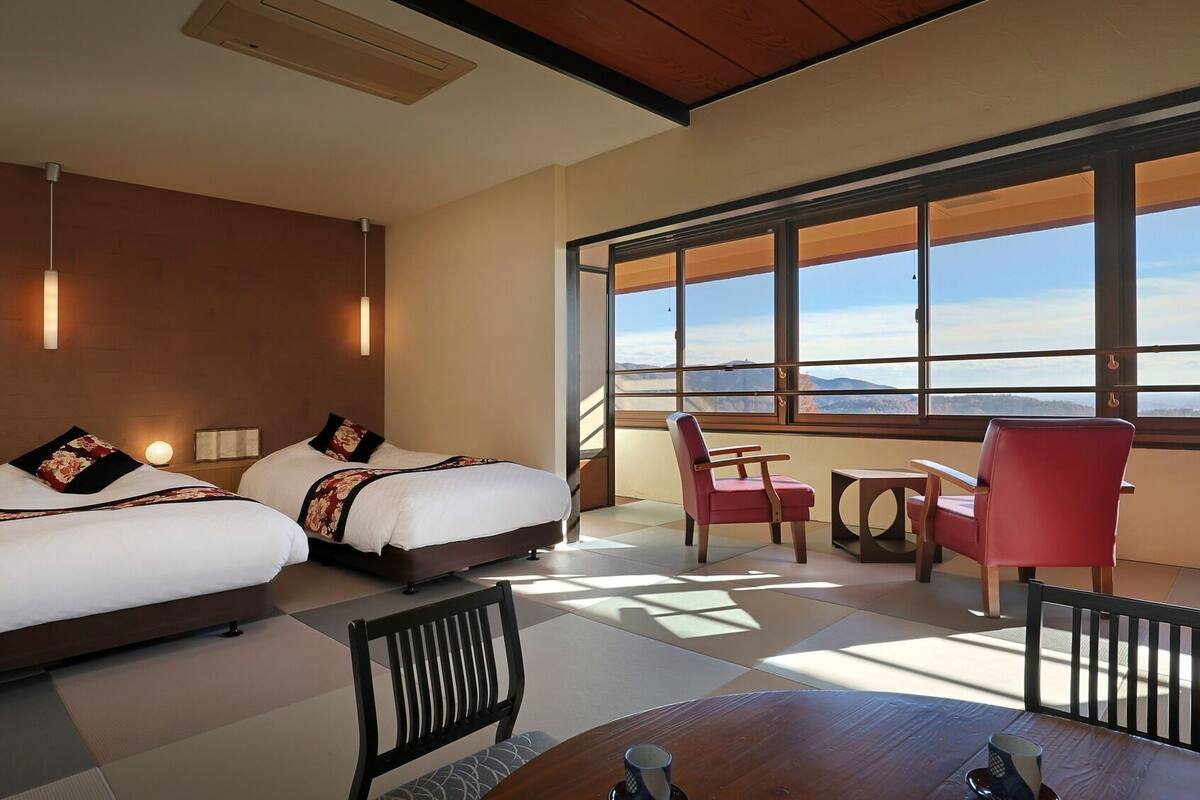 Une chambre d’hôtel avec deux lits, une table à manger, des chaises et de grandes fenêtres donnant sur une vue sur les montagnes.