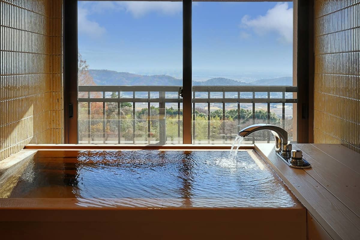 A bathroom with a large window, a bathtub, and a faucet.
