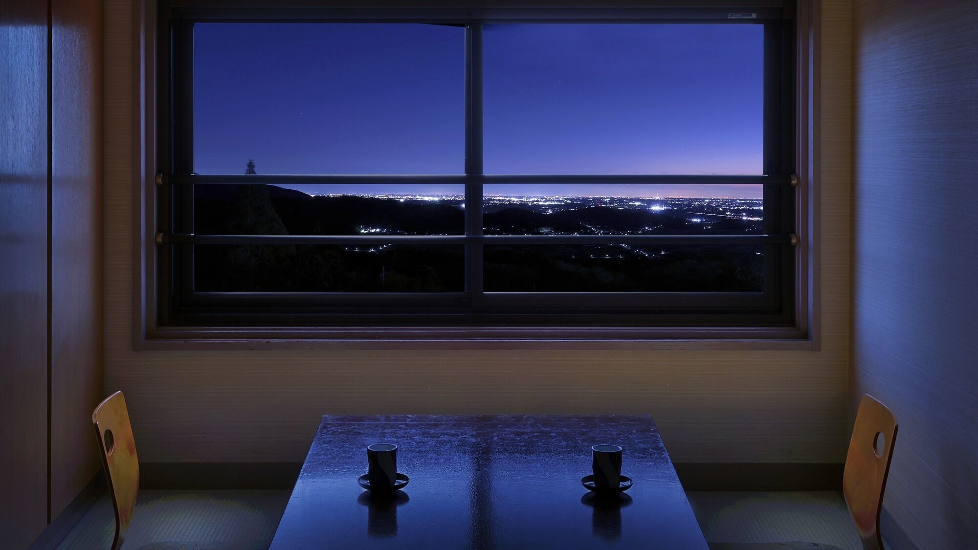Une pièce dotée d’une grande fenêtre donnant sur une vue panoramique de la ville la nuit.