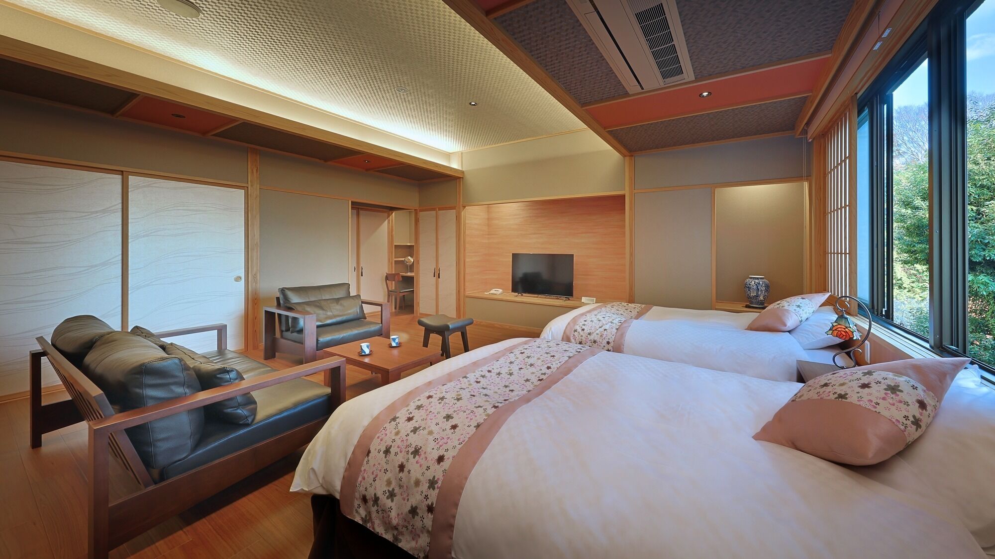 Une chambre d’hôtel moderne équipée de deux lits, d’un canapé, d’une télévision et d’une grande fenêtre donnant sur l’extérieur.
